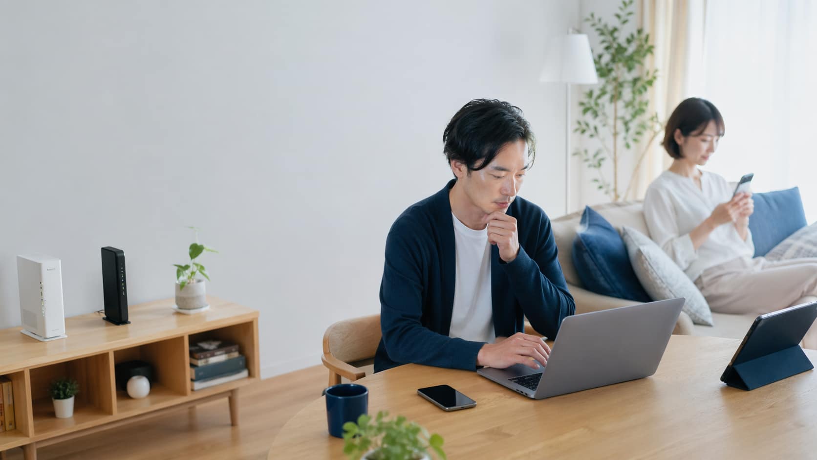 光回線機器があるリビングで、パソコンとスマホを使う男女